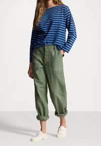 Blå och marinrandig långärmad topp, kombinerad med olivgröna cargobyxor och vita sneakers. Tyget verkar mjukt; byxorna har sidofickor.