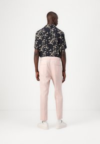 Kortärmad svart skjorta med vitt blommönster, kombinerad med ljusrosa byxor och vita sneakers, sedd bakifrån.