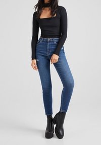 Svart långärmad topp med fyrkantig halsringning, ihopparat med blå högmidjade jeans. Outfitten kompletteras av kraftiga svarta plattformsskor.