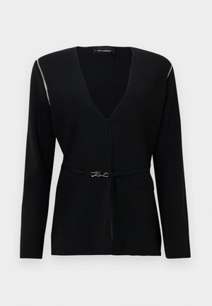 Čierny kardigán s hlbokým výstrihom do V a dlhými rukávmi, ozdobený strieborným zipsom na ramene a dekoratívnou páskou v páse.