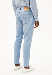 Jeans bleu clair avec une coupe slim, dotés d'une étiquette en cuir marron portant l'inscription "ARMEDANGELS" à la taille et de deux poches arrière.