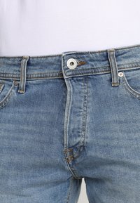 Jasnoniebieskie dżinsy o średnim stanie, z zapięciem na guzik i kontrastowym przeszyciem. Posiadają przednie kieszenie oraz subtelnie wyblakłą fakturę.