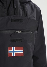 Czarna wodoodporna kurtka z zamkiem błyskawicznym, kieszenią zapinaną na zamek, akcentami na rzep i czerwoną naszywką z norweską flagą z przodu. Gładka tekstura, użytkowy design.