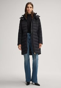 Zwarte pufferjas met een lang model, horizontale doorgestikte structuur en afneembare capuchon. Voorzien van ritssluiting en zijzakken.