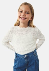 Hvid tekstureret langærmet skjorte med rund halsudskæring, parret med højtaljede blå denimjeans med sidelommer og knaplukning.