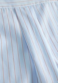 Hele sinine kangas peente vertikaalsete punaste triipudega ja ülemise serva lähedal keskmise voldi detail.