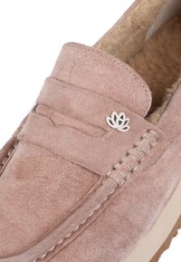 Mocasín de ante rosa con un interior suave, que presenta un emblema decorativo de loto plateado y acentos bordados a lo largo de los lados. Suela plana.