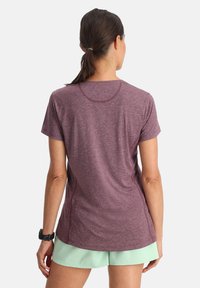Maglietta sportiva bordeaux a maniche corte, scollo rotondo e cuciture piatte; abbinata a pantaloni corti verde chiaro, che mostrano una vestibilità comoda.