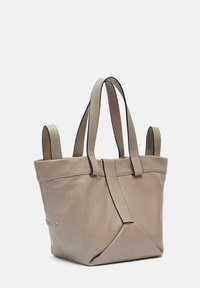 Beżowa skórzana torba tote o strukturalnym designie, z podwójnymi uchwytami u góry i dekoracyjnym złożonym akcentem z przodu. Gładka tekstura.