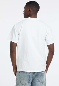 Biała bawełniana koszulka z krótkim rękawem, prosta fason, z okrągłym dekoltem. Zestawiona z jasnoniebieskimi dżinsami z tylnymi kieszeniami.