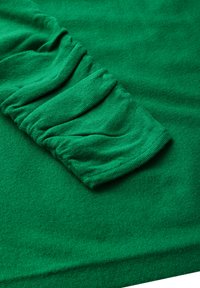 Grüner, texturierter Stoff mit gerafftem Detail an den Ärmeln. Weiches Material mit glatter Oberfläche und gleichmäßiger Farbe im gesamten Stoff.