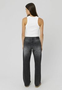Débardeur blanc à bretelles épaisses associé à un jean en denim noir taille haute et coupe droite, présentant une texture délavée et des poches arrière.