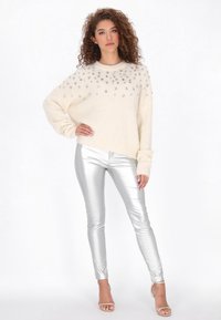 Crème gebreide trui met bedekte embellissementen, gecombineerd met glanzende zilveren leggings en strappy hakken. Zachte textuur, relaxte pasvorm.