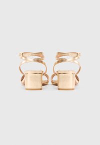 Gold heeled sandals with a block heel, featuring crisscross straps and a smooth metallic finish. Simple design with adjustable ankle straps.