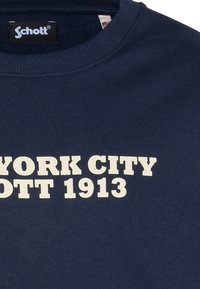 Sudadera de algodón azul marino con cuello redondo. Presenta un texto audaz en color crema: "NEW YORK CITY SCHOTT 1913." Textura suave, diseño clásico.