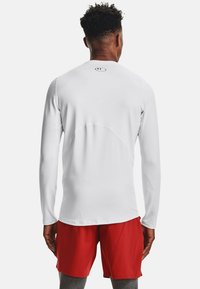 Langärmliges Shirt in Weiß mit einem runden Ausschnitt und nahtlosen Schultern. Trägt dazu rote Shorts, die ein sportliches Design zur Schau stellen.