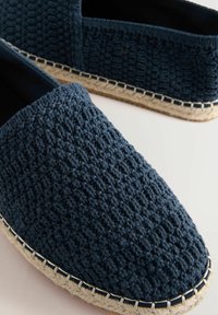 Zapatos slip-on de color azul marino con suela de yute estilo espadrille y costuras blancas, que cuentan con una parte superior texturizada y puntera redonda.