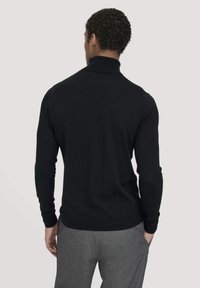 Schwarzer Rollkragenpullover mit langen Ärmeln, weichem Material, slim fit und geripptem Manschettendesign, kombiniert mit grauen Hosen.