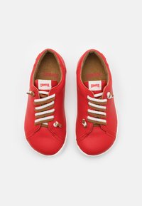 Czerwone skórzane sneakersy z białymi sznurowadłami i brązowymi akcentami, zaokrąglony czubek i teksturowana wkładka. Nazwa marki "Camper" widoczna na języku.