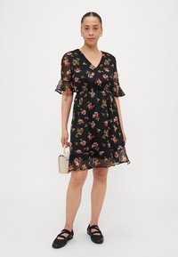 Robe noir à fleurs avec des manches courtes et transparentes, taille froncée ; présente des motifs de fleurs roses et jaunes, longueur genou avec un ourlet volanté.