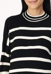 Svart-hvitt stripete genser med ribbestruktur, med brede horisontale striper og høy hals-design med doble stripe-elementer.