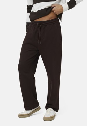 Uomo con pantaloni neri con coulisse e scarpe da ginnastica bianche, che solleva una maglietta a righe bianca e nera per mostrare l'addome.