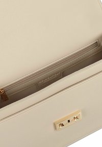 Interno di una borsa in pelle beige con una tasca con zip, una texture liscia, dettagli in hardware dorato e cuciture lungo i bordi.