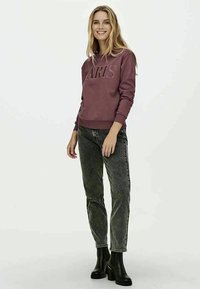 Μαραoon φούτερ με ανάγλυφο κείμενο "PARIS", συνδυασμένο με ξεθωριασμένο γκρι τζιν και μαύρες γαλότσες μέχρι τον αστράγαλο. Μαλακό υλικό με ραμμένα μανίκια.