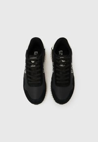 Fekete sportcipők, sima szintetikus és texturált velúr anyagok kombinációjával, kontrasztos fehér díszítésekkel és kerek cipőfűzőkkel.