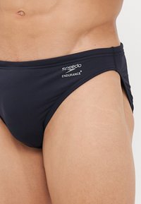 Fekete úszónadrág sima szövetből, varrott élekkel, fehér "Speedo" és "Endurance+" logókkal a derékpánton.