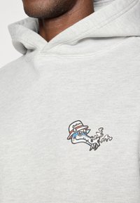 Γκρι φούτερ από βαμβάκι με μικρό κεντημένο γραφικό ενός στιλιζαρισμένου ζώου με κ�απέλο, που καπνίζει, στην αριστερή περιοχή του στήθους.