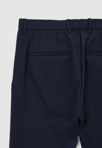 Pantaloni navy con un tessuto liscio e strutturato. Presentano una parte anteriore piatta, passanti per cintura e due tasche posteriori. Dettagli di sartoria intricati visibili.