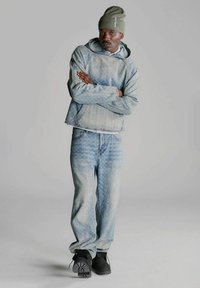 Completo in denim con felpa blu a fantasia e jeans abbinati. Pantaloni larghi, abbinati a calzature nere.