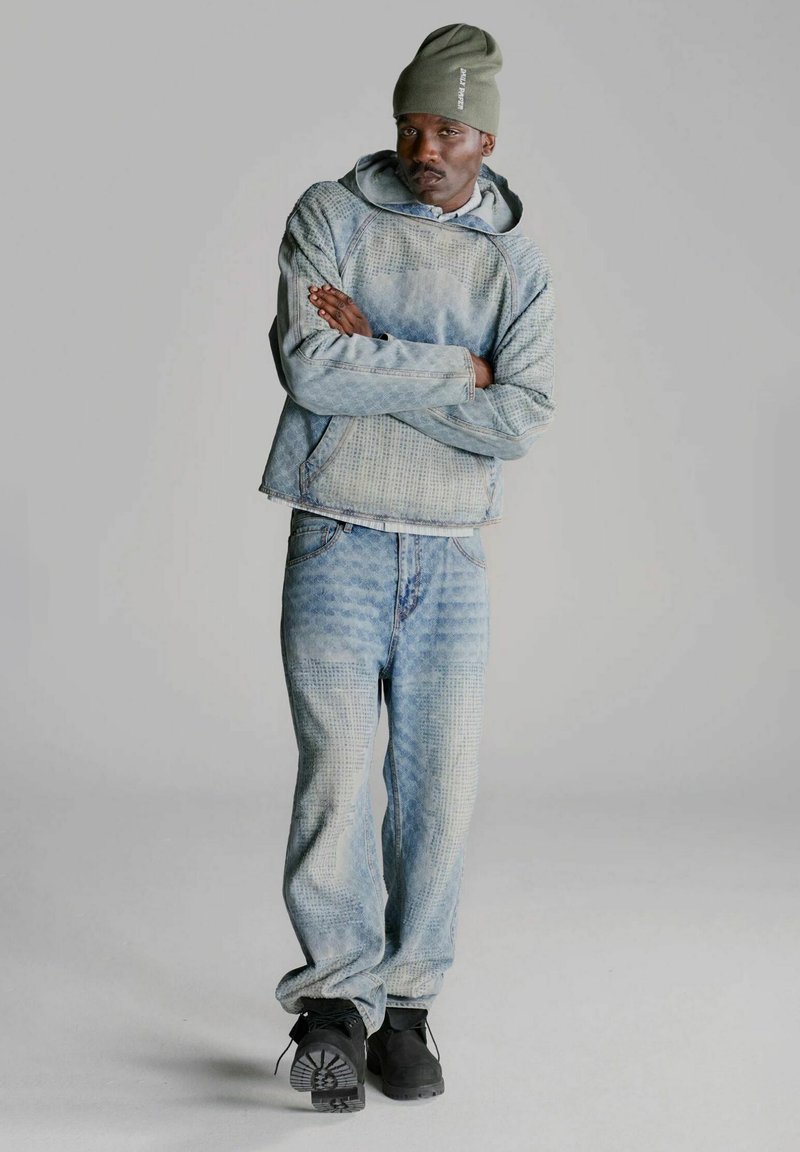 Completo in denim con felpa blu a fantasia e jeans abbinati. Pantaloni larghi, abbinati a calzature nere.