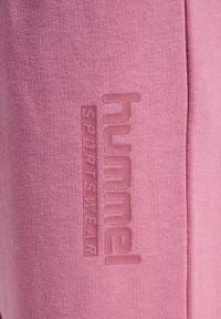 Sudadera rosa hecha de tela suave con un logo texturizado en un tono ligeramente más oscuro de rosa. Diseño sencillo y sin adornos, con forma ajustada.
