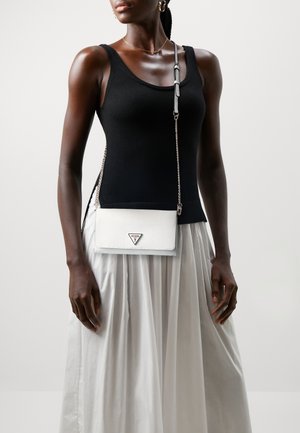 Sac bandoulière blanc avec une surface texturée, une quincaillerie argentée et un logo triangulaire. Porté avec un débardeur noir et une jupe blanche.