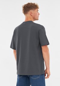 Szary bawełnowy T-shirt z krótkimi rękawami, okrągłym dekoltem i luźnym krojem. Posiada gładką fakturę, prosty krój i brak widocznych wzorów.