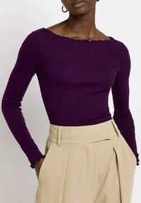 Długi rękaw top w głębokim fioletowym kolorze, z prążkowanej tekstury, z falbaniastym dekoltem. Połączony z beżowymi, plisowanymi spodniami z wysokim stanem.