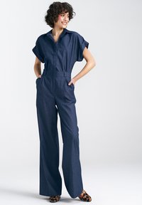 Dżinsowy kombinezon z krótkimi rękawami, kołnierzykiem, zamek błyskawiczny z przodu i paskiem w talii. Ciemnoniebieski kolor, szerokie nogawki. Uzupełniony butami w leopardzimprint.