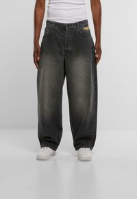 Vaqueros negros de denim holgados con un diseño desteñido, que cuentan con dos bolsillos delanteros y un logo en la cinturilla. Combinados con zapatillas blancas.