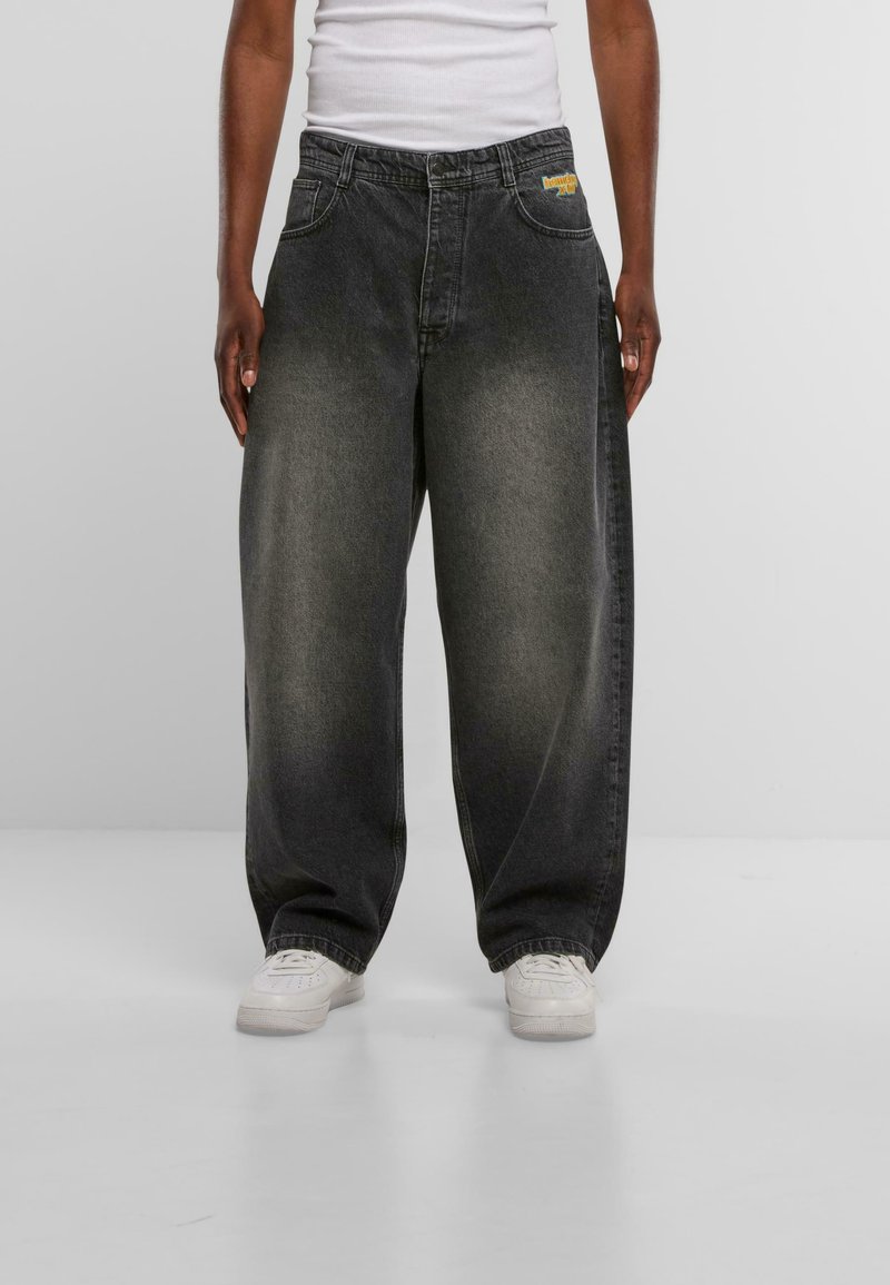 Vaqueros negros de denim holgados con un diseño desteñido, que cuentan con dos bolsillos delanteros y un logo en la cinturilla. Combinados con zapatillas blancas.