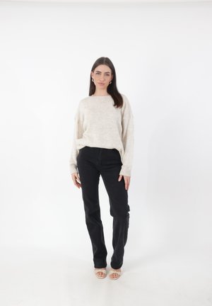Lichte beige oversized trui, gebreide textuur, geribde manchetten; gecombineerd met zwarte rechte jeans en naakte open teen hakken.