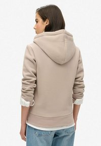 Beige hoodie met textuur, opgerolde mouwen en een zichtbaar wit shirt eronder. Casual pasvorm met een relaxte silhouet.