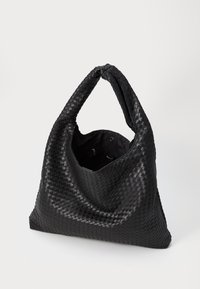 Svart vävd hobo-väska med en överdimensionerad form, mjuk textur och ett enda vridet handtag. Interiören inkluderar en dragkedjeficka.