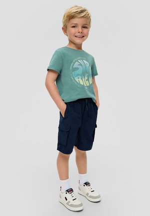 Grüne T-Shirt mit "Super" Grafik, kombiniert mit navy Cargo-Shorts. Weiße Sneakers mit roten und blauen Akzenten. Gerade geschnittenes, lässiges Design.