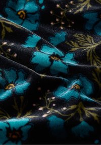 Schwarzer Stoff mit einem floralen Muster, das türkisfarbene Blumen und grüne Blätter sowie kleine pinke Akzente zeigt, hat eine samtige Textur.