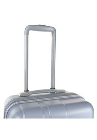 Maleta rígida plateada con textura acanalada, mango retráctil y cierre de cremallera. Cuenta con un robusto asa superior para facilitar el levantamiento.