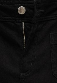 Čierne džíny z denimu s čiastočne rozopnutým strieborným zipsom a kovovým gombíkom s vyrazeným textom na páse.