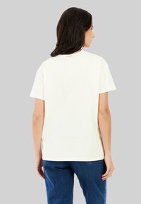 Crème t-shirt met korte mouwen van katoen, met een klein rood logo op de achterkant van de halslijn, gecombineerd met blauwe denim jeans.