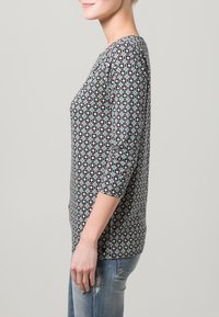 Maglia a maniche lunghe con motivo geometrico nei toni del nero, teal e bianco. Realizzata in tessuto morbido, presenta una vestibilità comoda e un collo rotondo.